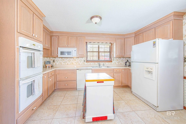 kitchen with a sink, white appliances, and light brown cabinetry