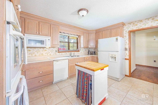 kitchen featuring light brown cabinets, white appliances, butcher block counters, and a sink