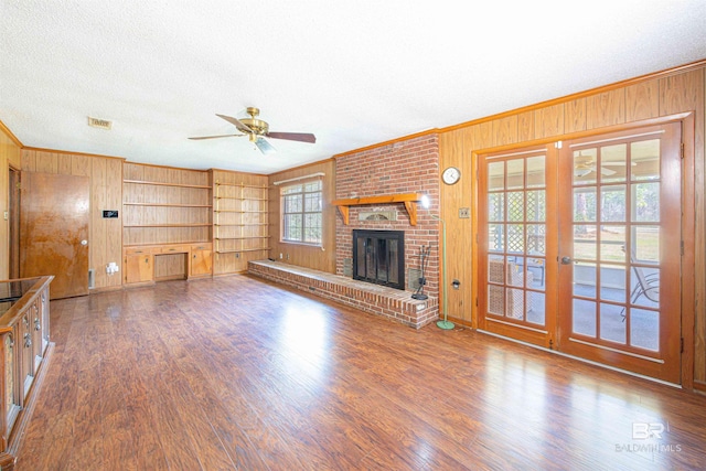 unfurnished living room with wood walls, crown molding, a ceiling fan, and wood finished floors