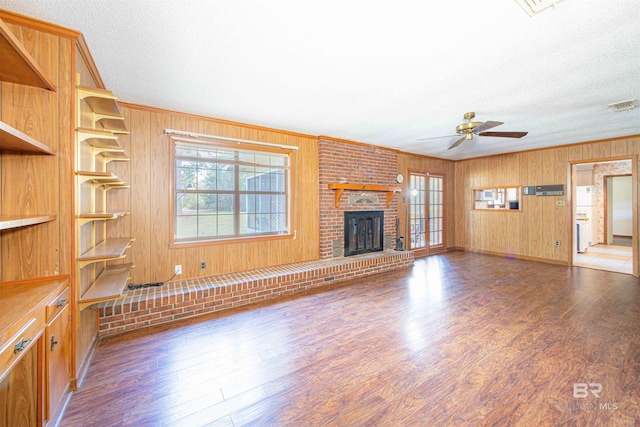 unfurnished living room with visible vents, a brick fireplace, crown molding, ceiling fan, and wood finished floors