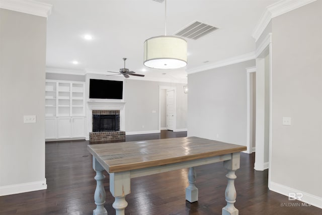 unfurnished dining area with dark wood-type flooring, crown molding, a brick fireplace, built in features, and ceiling fan