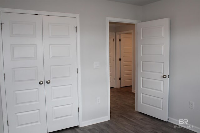 unfurnished bedroom featuring a closet, dark wood-style flooring, and baseboards