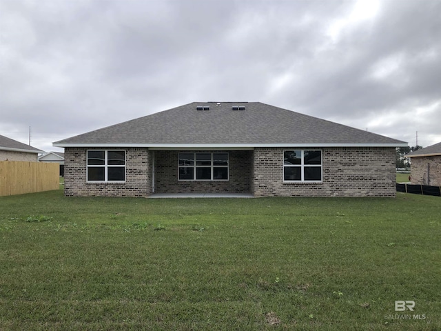 rear view of property with brick siding, a lawn, a shingled roof, and fence