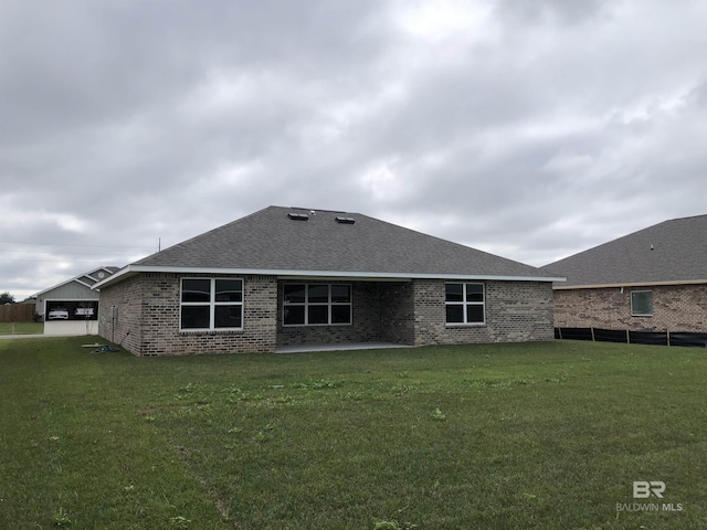 back of house with a yard, roof with shingles, a patio, and brick siding