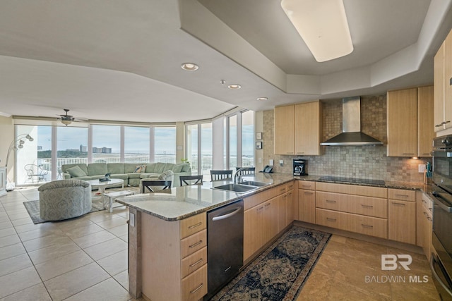 kitchen with light brown cabinets, wall chimney exhaust hood, light stone countertops, and sink