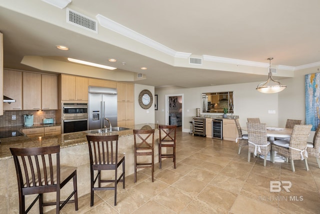 kitchen with light brown cabinets, appliances with stainless steel finishes, wine cooler, a kitchen bar, and hanging light fixtures