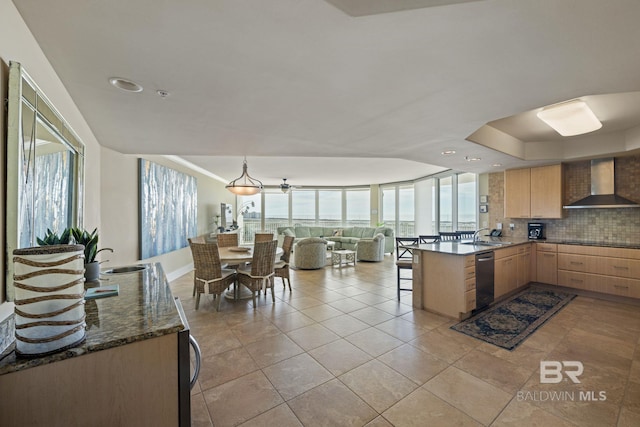 kitchen featuring dark stone counters, wall chimney range hood, a wealth of natural light, and light brown cabinetry