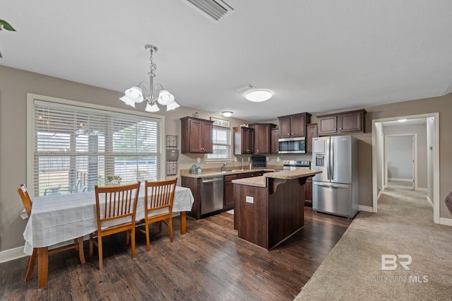 kitchen with appliances with stainless steel finishes, a center island, pendant lighting, dark brown cabinets, and an inviting chandelier