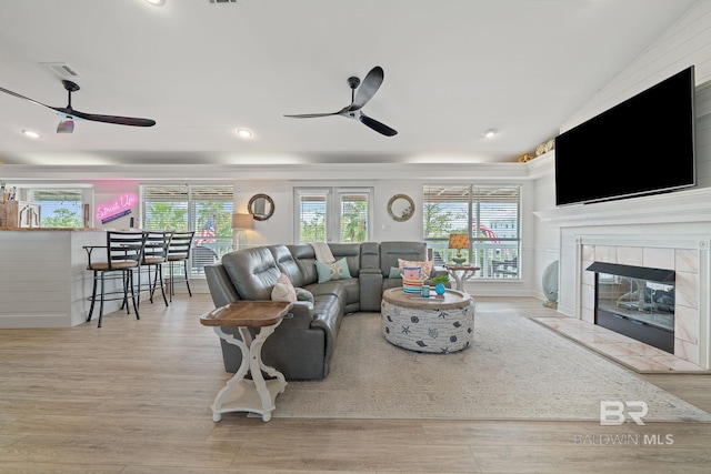 living room with ceiling fan, a healthy amount of sunlight, a tile fireplace, and light hardwood / wood-style flooring