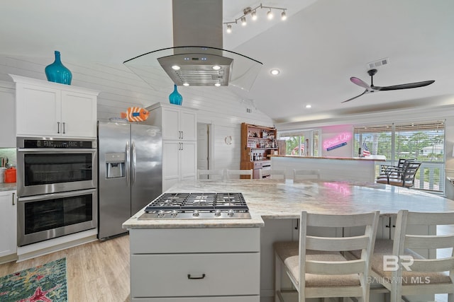 kitchen with vaulted ceiling, white cabinets, a kitchen bar, island exhaust hood, and stainless steel appliances