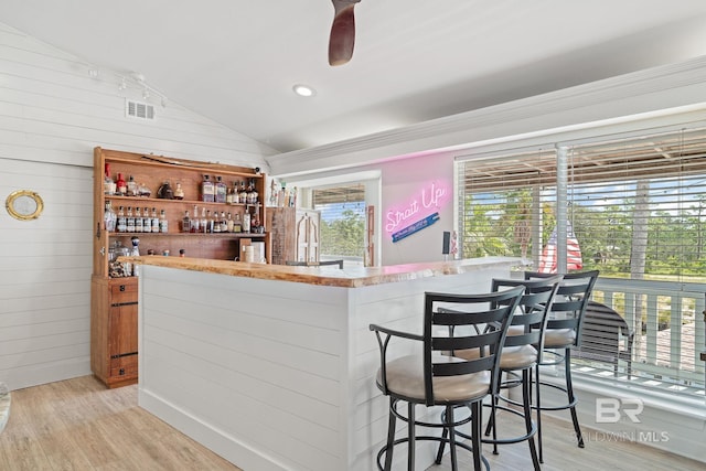 bar featuring ceiling fan, lofted ceiling, light hardwood / wood-style floors, and wood walls