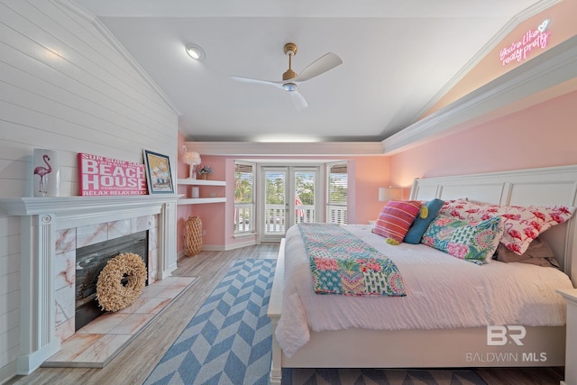 bedroom featuring lofted ceiling, access to outside, a tile fireplace, and light wood-type flooring