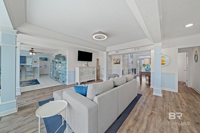 living room with decorative columns, ornamental molding, ceiling fan, a textured ceiling, and light wood-type flooring