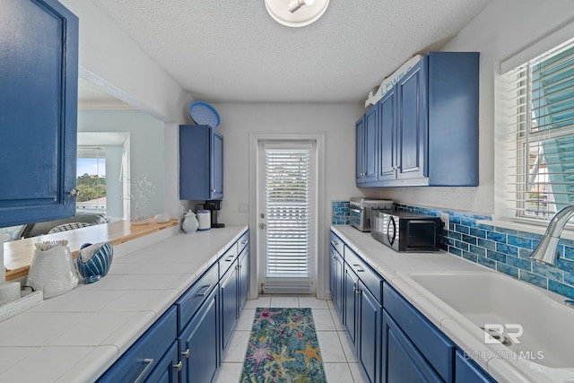 kitchen with sink, tile countertops, light tile patterned flooring, and blue cabinets