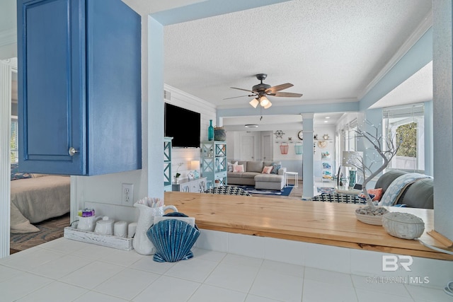 tiled living room with ornate columns, crown molding, ceiling fan, and a textured ceiling