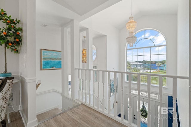 corridor with a notable chandelier, hardwood / wood-style flooring, and vaulted ceiling