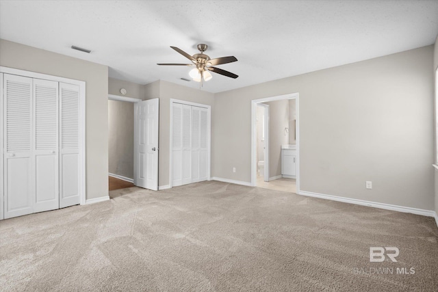 unfurnished bedroom with connected bathroom, multiple closets, light colored carpet, and ceiling fan