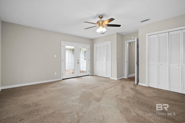 unfurnished bedroom featuring two closets, ceiling fan, a textured ceiling, french doors, and light colored carpet