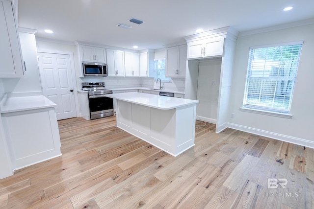 kitchen featuring white cabinetry, light hardwood / wood-style floors, a kitchen island, appliances with stainless steel finishes, and backsplash