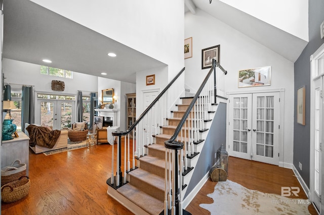 staircase featuring high vaulted ceiling, french doors, and hardwood / wood-style floors