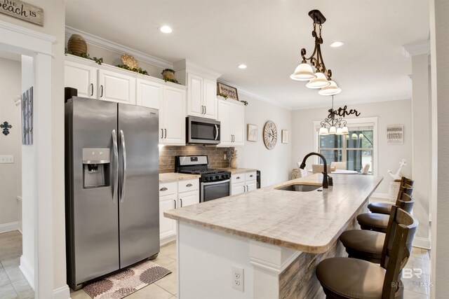 kitchen with appliances with stainless steel finishes, decorative light fixtures, white cabinetry, an island with sink, and sink