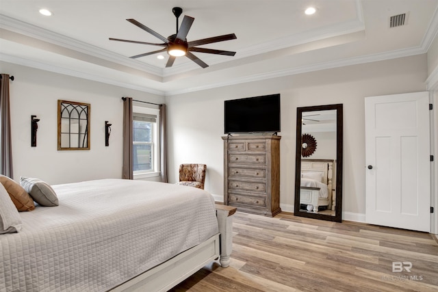 bedroom with crown molding, light wood-type flooring, ceiling fan, and a tray ceiling