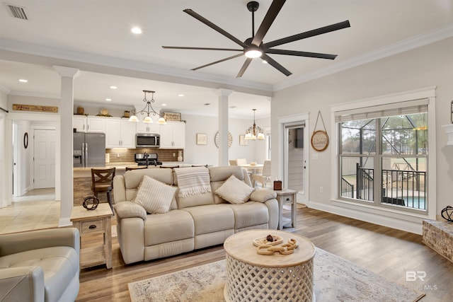 living room featuring ceiling fan with notable chandelier, light hardwood / wood-style flooring, ornamental molding, and ornate columns