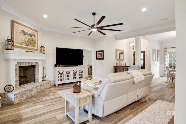 living room featuring crown molding, a fireplace, ceiling fan with notable chandelier, and light wood-type flooring