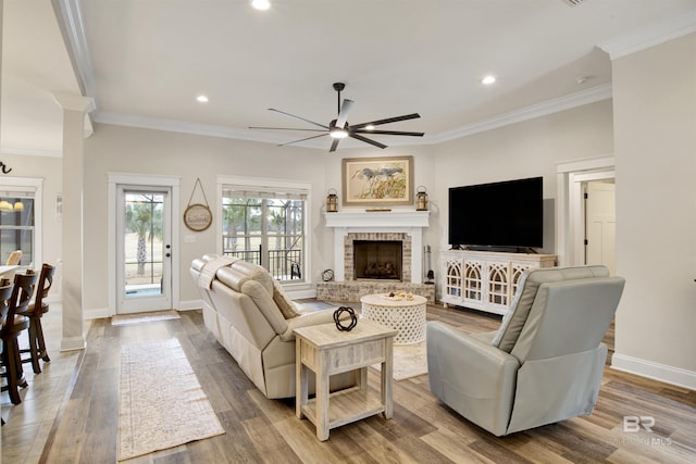 living room with ornate columns, a fireplace, hardwood / wood-style flooring, ornamental molding, and ceiling fan