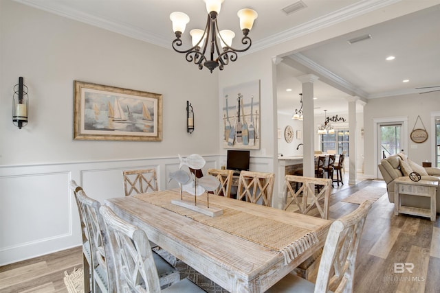 dining room with hardwood / wood-style flooring, ornamental molding, a chandelier, and decorative columns