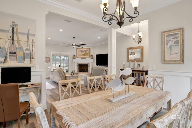 dining area with ornate columns, crown molding, a brick fireplace, hardwood / wood-style floors, and ceiling fan with notable chandelier