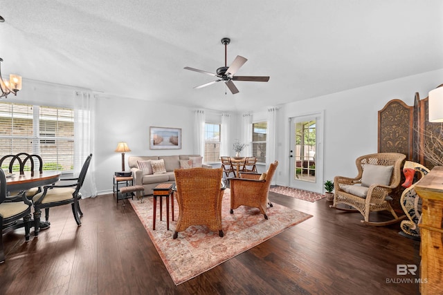 living room with ceiling fan with notable chandelier, dark wood-type flooring, and a textured ceiling