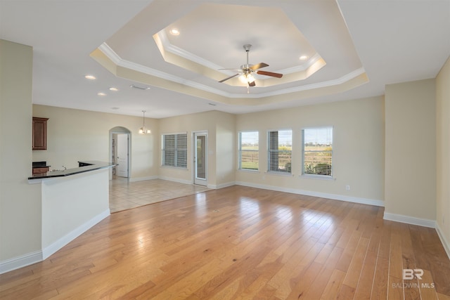 unfurnished living room featuring ceiling fan, light hardwood / wood-style flooring, crown molding, and a tray ceiling