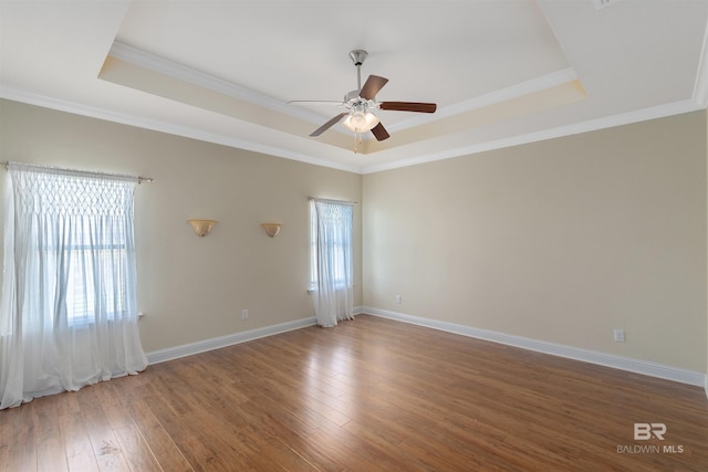 empty room featuring a raised ceiling, dark hardwood / wood-style floors, ornamental molding, and a wealth of natural light