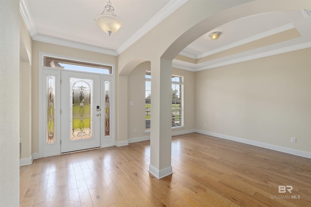 foyer entrance with ornamental molding, light wood-type flooring, and a raised ceiling