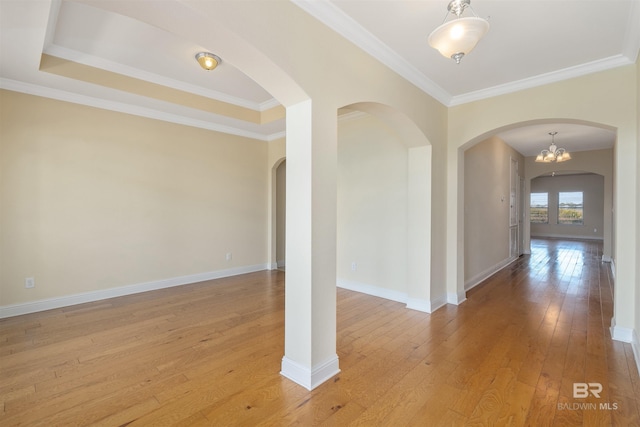 empty room featuring a notable chandelier, light wood-type flooring, and ornamental molding