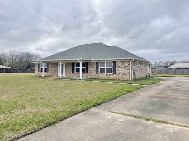 view of front of house with brick siding, roof with shingles, fence, and a front yard