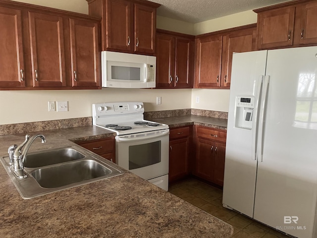 kitchen featuring white appliances, dark countertops, a textured ceiling, dark tile patterned floors, and a sink