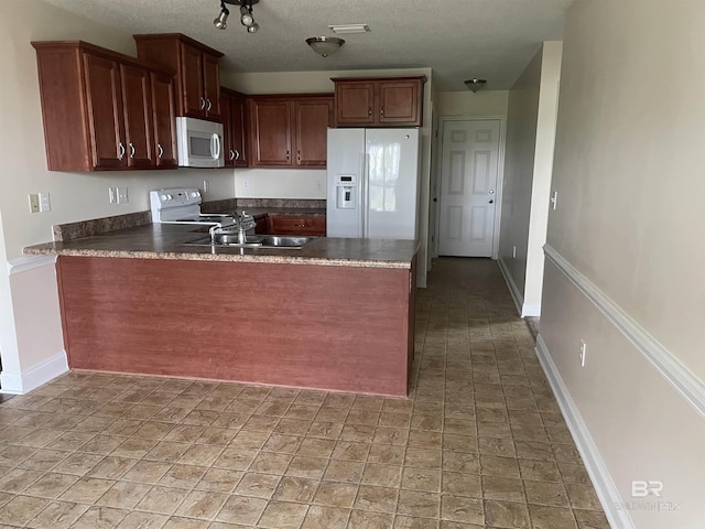 kitchen with dark countertops, a sink, white appliances, a peninsula, and baseboards