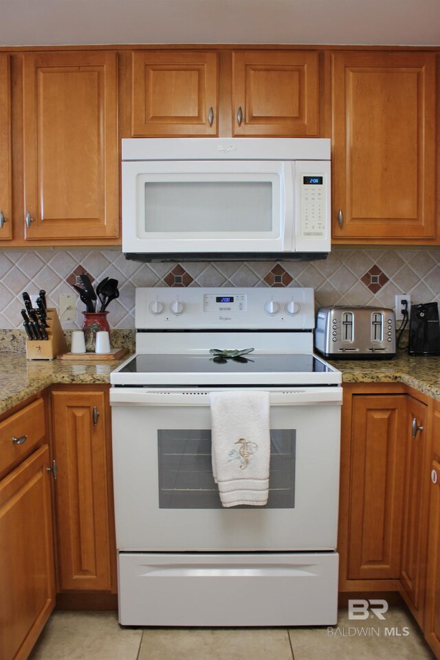 kitchen featuring light tile patterned flooring, light stone countertops, white appliances, and backsplash