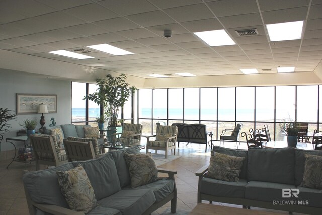 tiled living room featuring a paneled ceiling, a water view, and a beach view