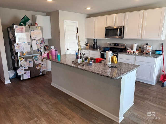 kitchen with appliances with stainless steel finishes, an island with sink, white cabinets, dark hardwood / wood-style flooring, and dark stone counters