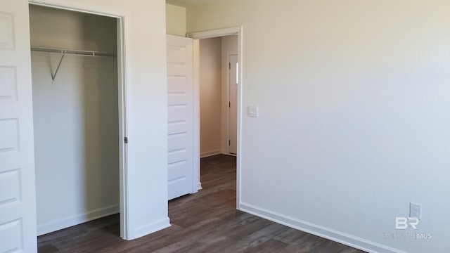 unfurnished bedroom with dark wood-style floors, baseboards, and a closet