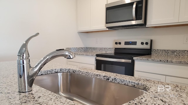 kitchen featuring stainless steel appliances, light stone counters, a sink, and white cabinets