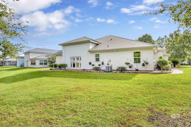 back of house with central AC unit, a lawn, and metal roof