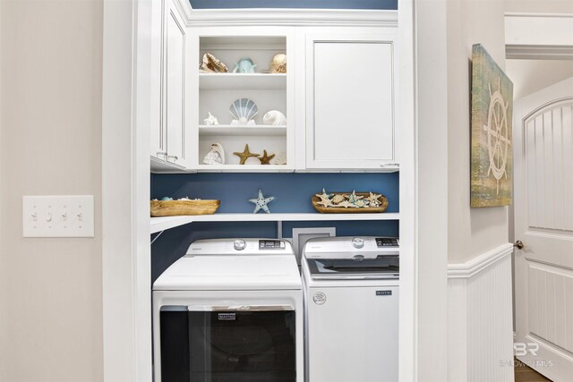 clothes washing area featuring a wainscoted wall, cabinet space, and independent washer and dryer