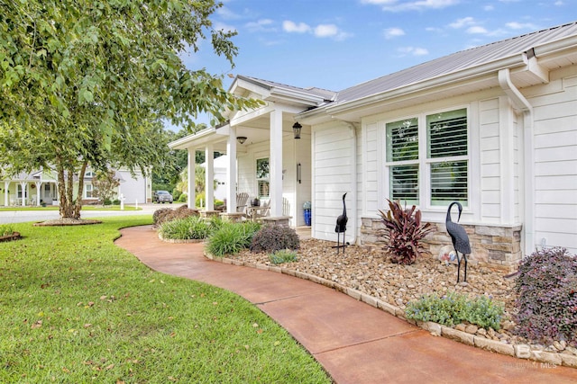 entrance to property featuring a yard, covered porch, stone siding, and metal roof