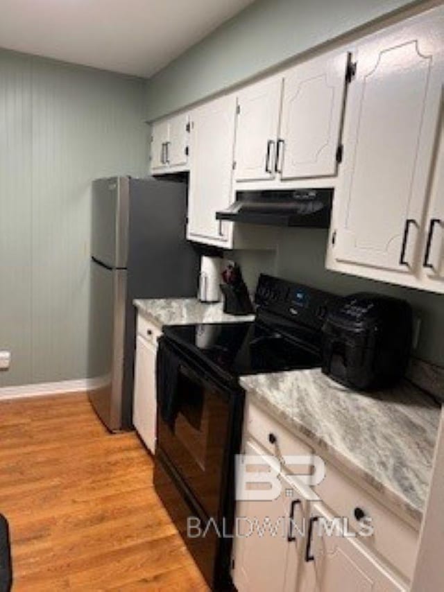 kitchen with under cabinet range hood, black range with electric cooktop, freestanding refrigerator, white cabinets, and light wood finished floors