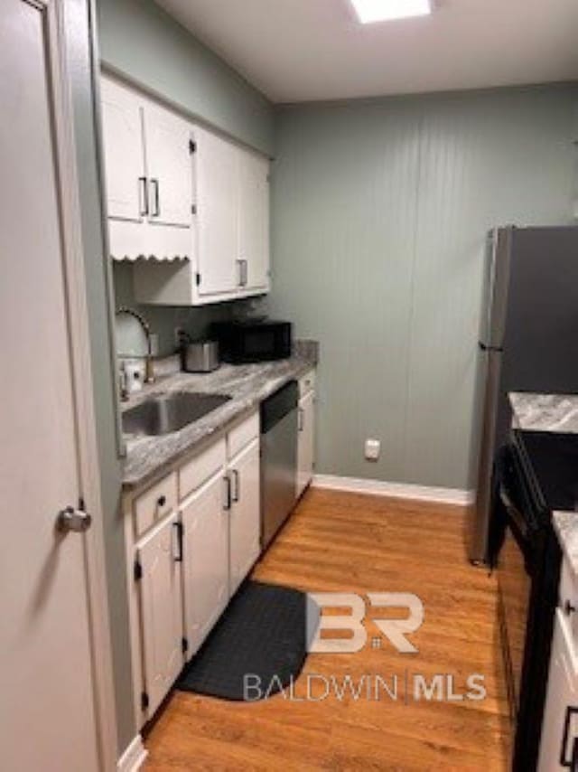 kitchen featuring light wood-type flooring, light countertops, white cabinets, black appliances, and a sink