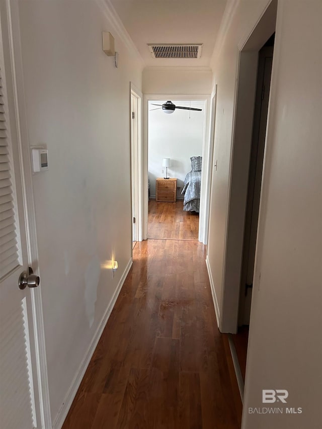 hallway featuring ornamental molding, dark wood-style floors, visible vents, and baseboards